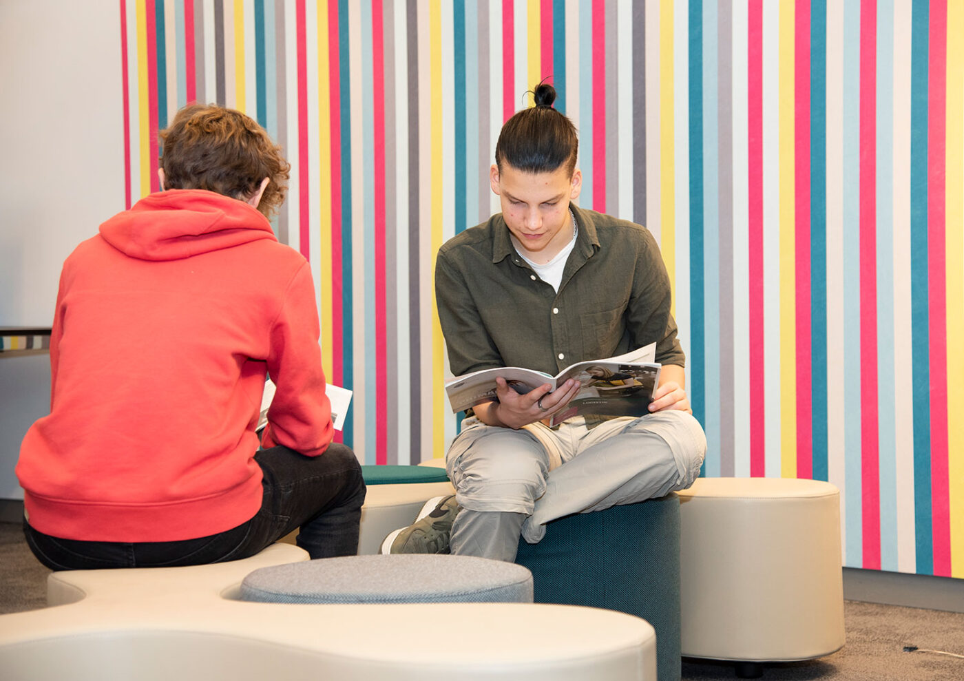 In einer Infothek sitzen zwei Jugendliche vor einer farbig gestreiften Wand und studieren Infomaterialien.